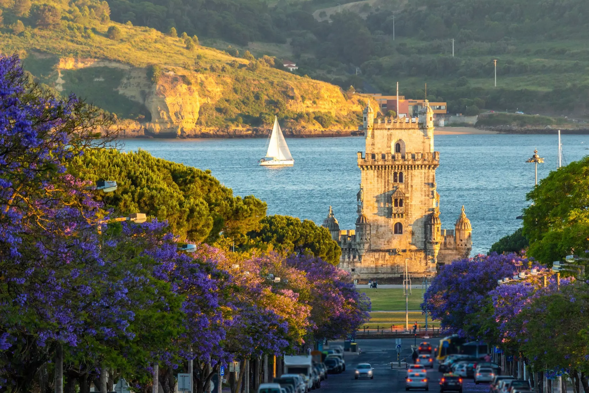 Belem Tower, Jacaranda Blooming Purple Blue Trees and Sailboat on Sunny Evening. Golden Hour. Lisbon, Portugal., License Type: media, Download Time: 2025-07-17T16:52:26.000Z, User: katelyn.perry_lonelyplanet, Editorial: false, purchase_order: 65050 - Digital Destinations and Articles, job: WIP, client: WIP, other: Katelyn Perry