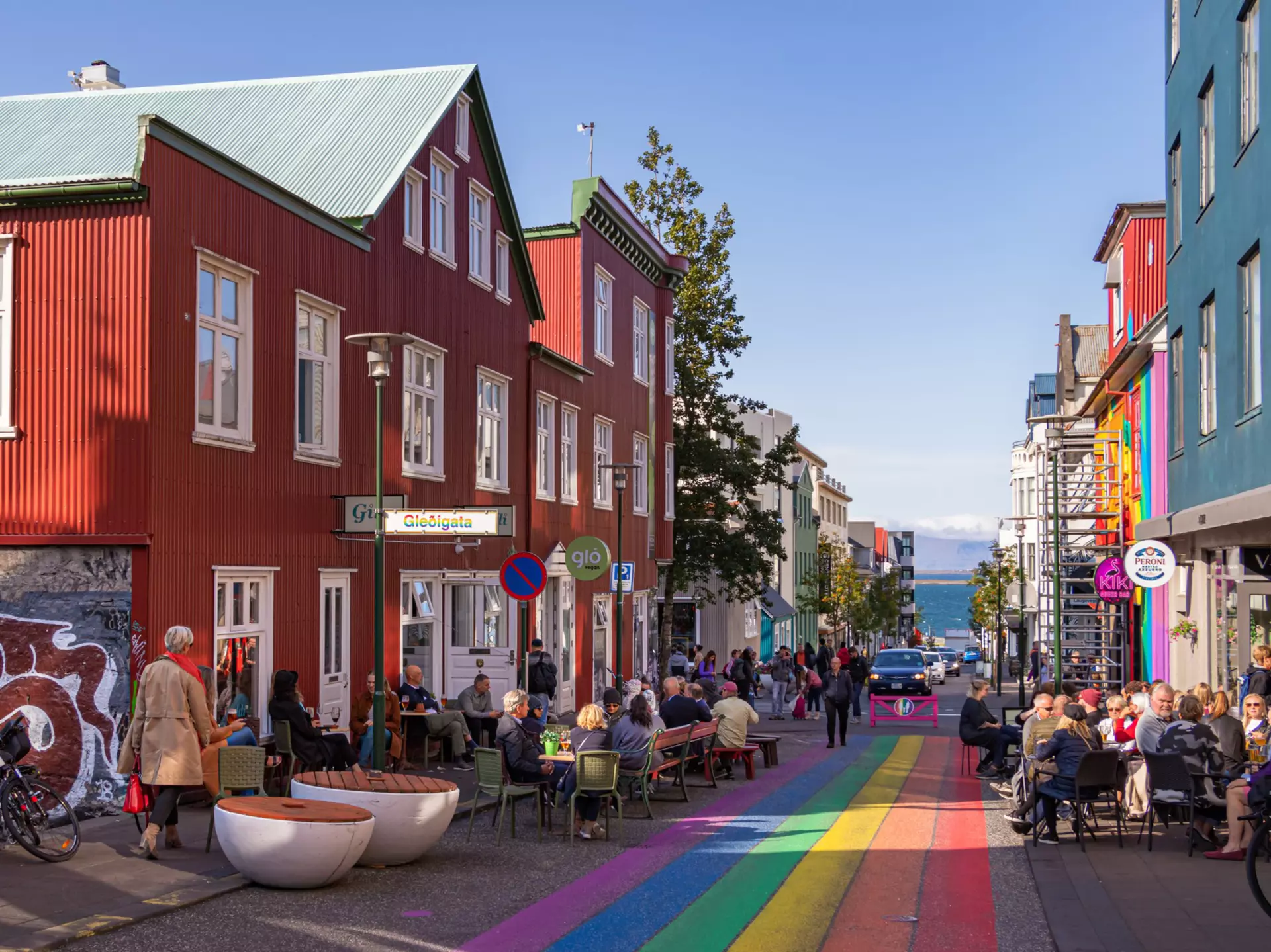 People sit at outdoor cafes on a street with rainbow stripes painted down the middle.