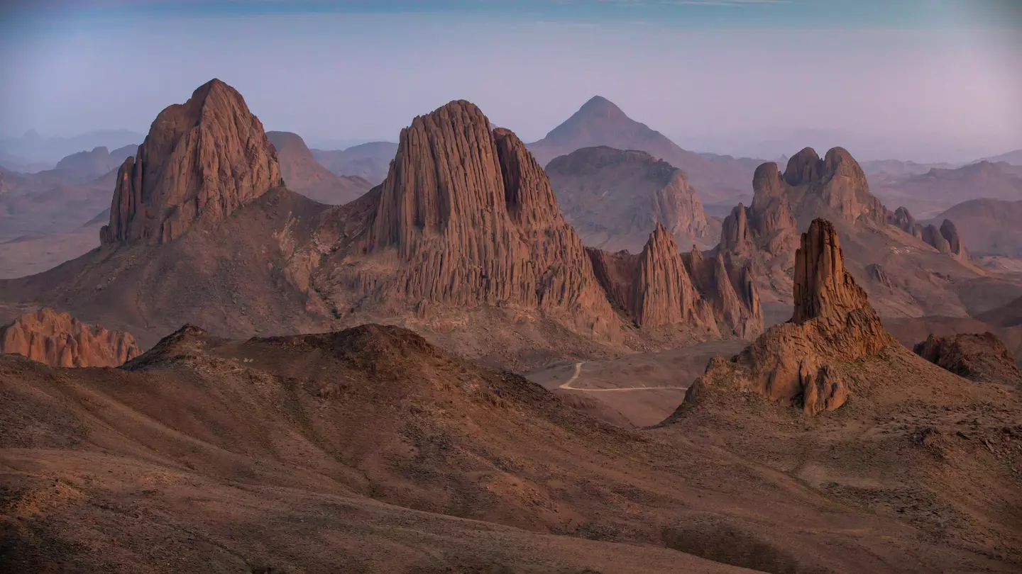 Rugged mountain peaks in a desert as the light fades casting a pink glow across the sky.