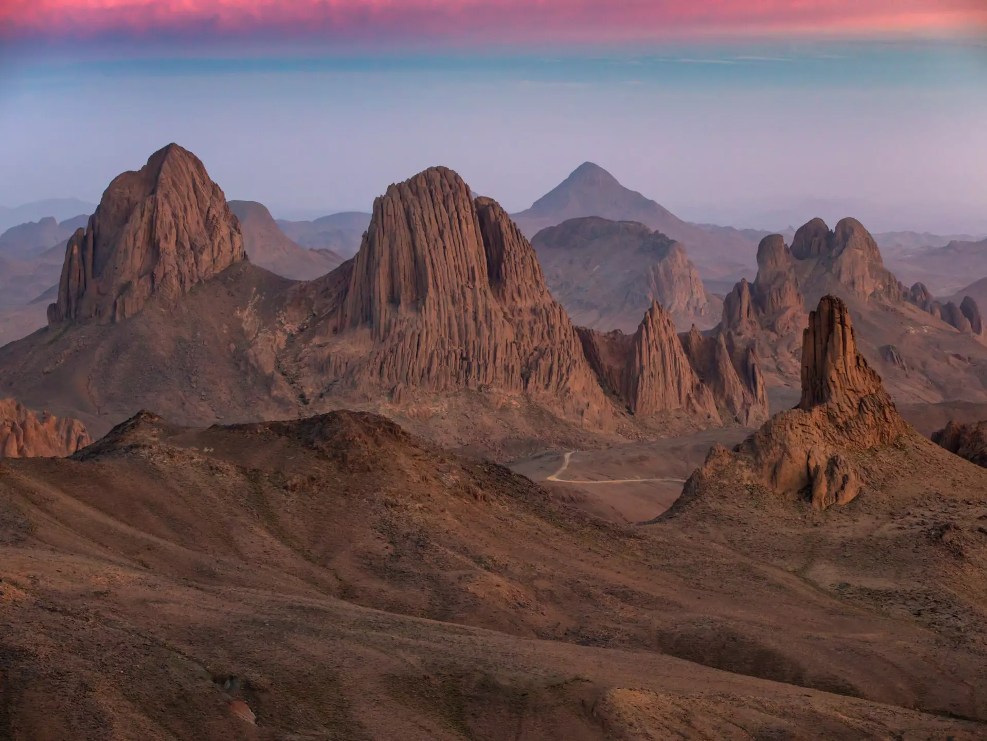 Rugged mountain peaks in a desert as the light fades casting a pink glow across the sky.