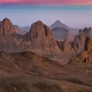 Rugged mountain peaks in a desert as the light fades casting a pink glow across the sky.