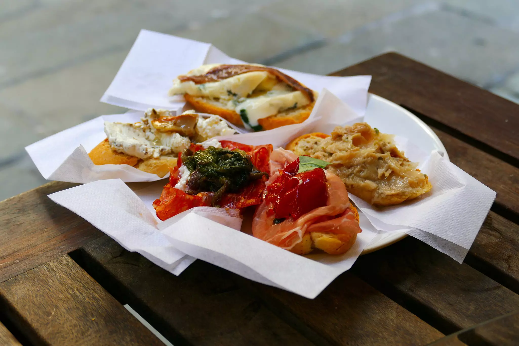 A plate of breads prepared with a variety of toppings atop a wooden table