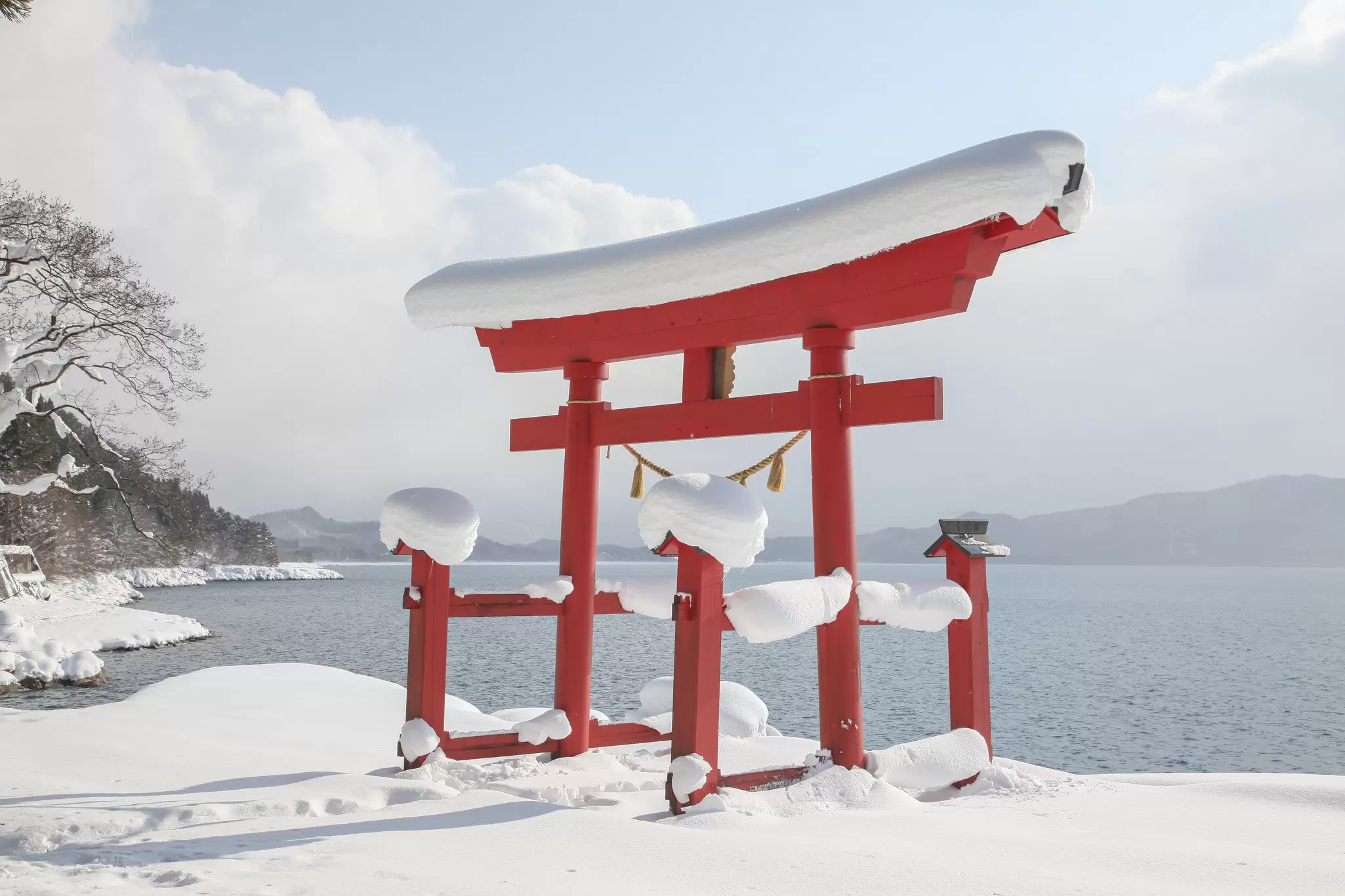 A red temple gate by a lake in a snowy landscape.