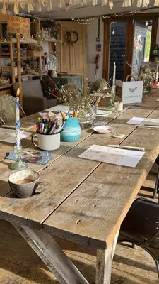 A long wooden table with many chairs on either side and craft supplies on the table and on shelves by the wall.