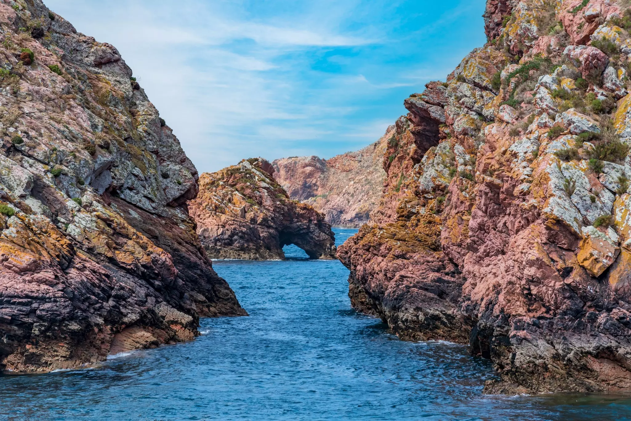 A natural rock arch out at sea near red-rock cliffs