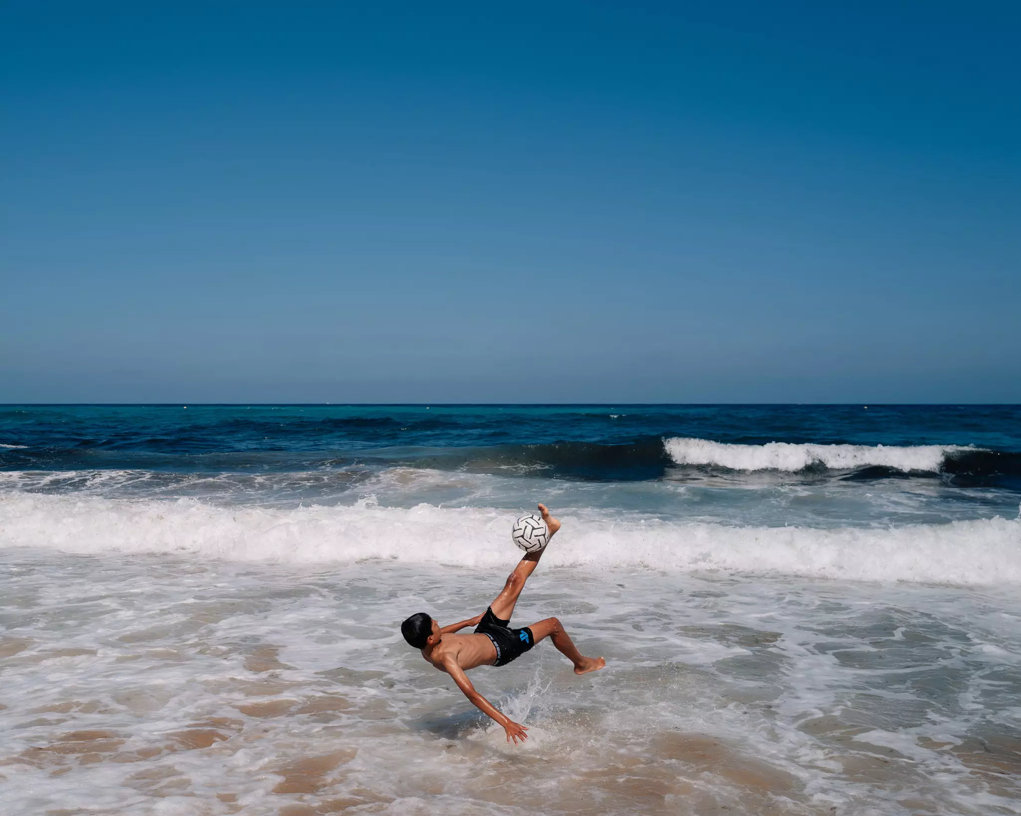 A young boy attempts a bicycle kick in the surf on a beach in Tangier, Morocco.