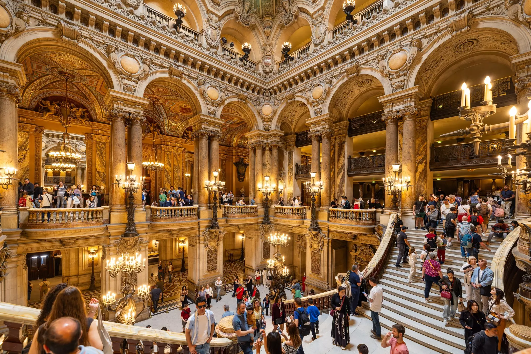 People on a staircase in an atrium with golden accents.