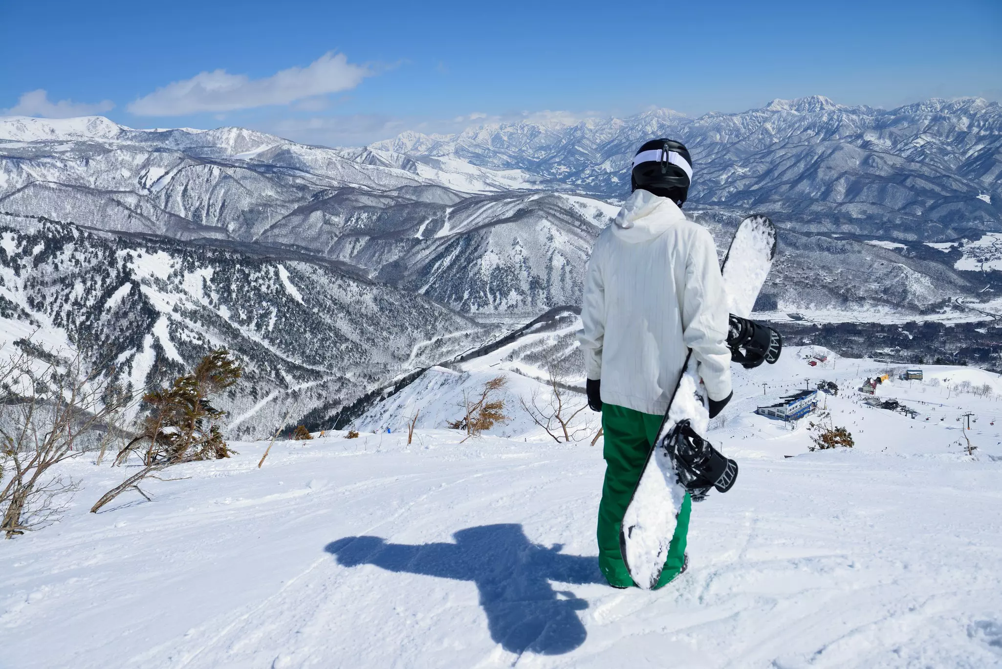 Man stands at the top of a snowy mountain with his snowboard in hand.