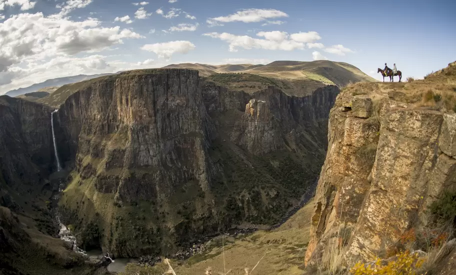 Two horse riders on a cliff edge above the deep Maletsunyane gorge and its tall waterfall near Semonkong, Lesotho