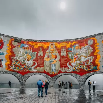 Curved tiled mural dated 1783 and 1983 of a woman, child and horsemen, above stone arches where visitors stand in fog