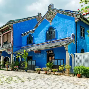 Indigo-blue facade with ornate gables and potted plants at Cheong Fatt Tze Blue Mansion in George Town, Penang