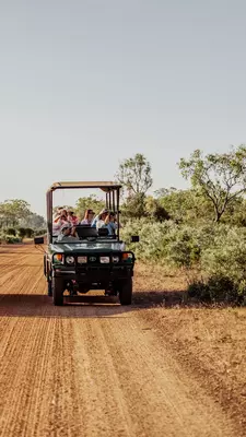 People ride in an open jeep on a red dirt road.