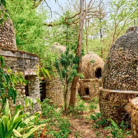 Stone buildings built close together with round stone and thatch roofs in a forested area.