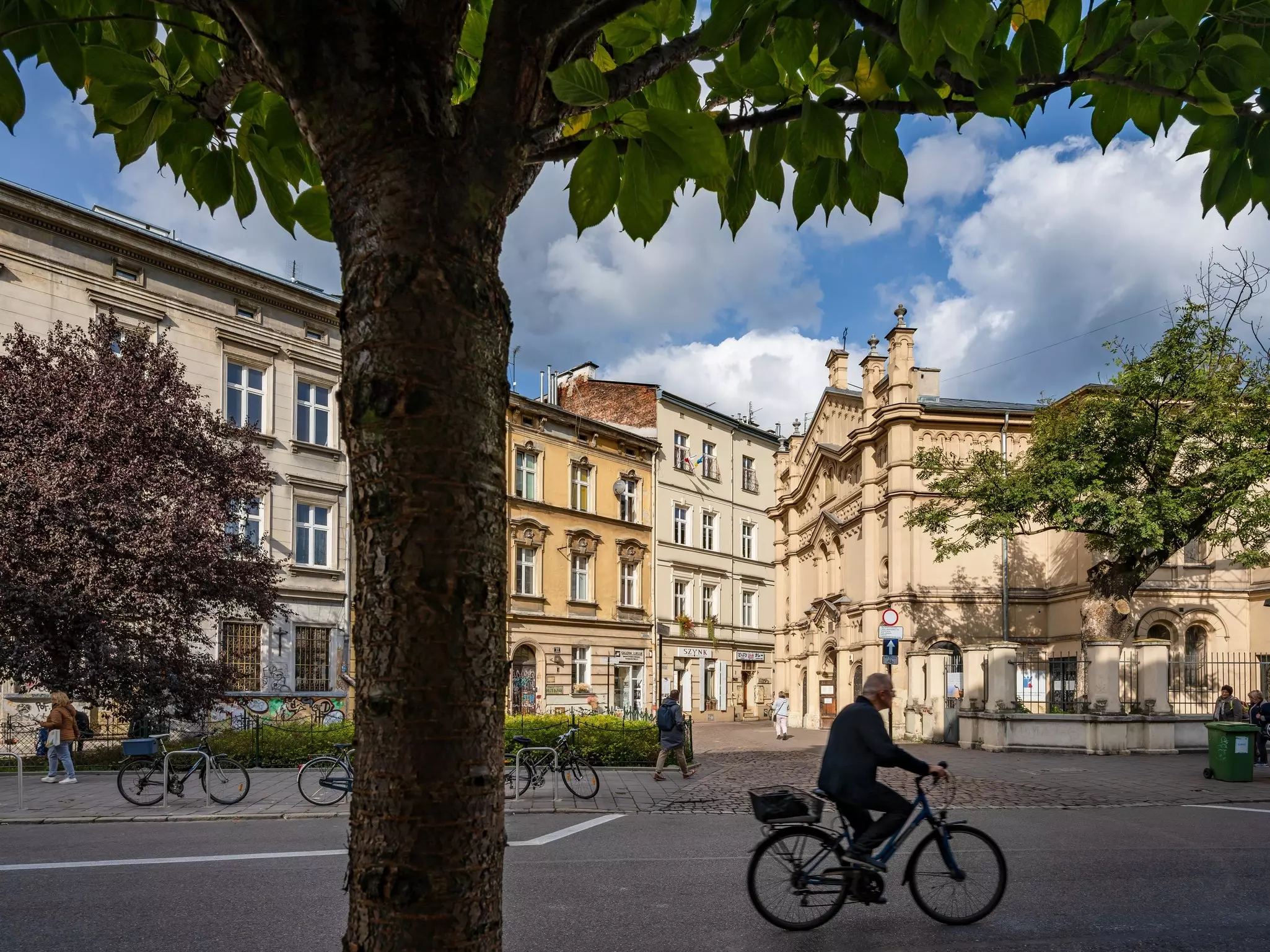 A person riding a bicycle through a square in shadow; the buildings in the background are in the light.