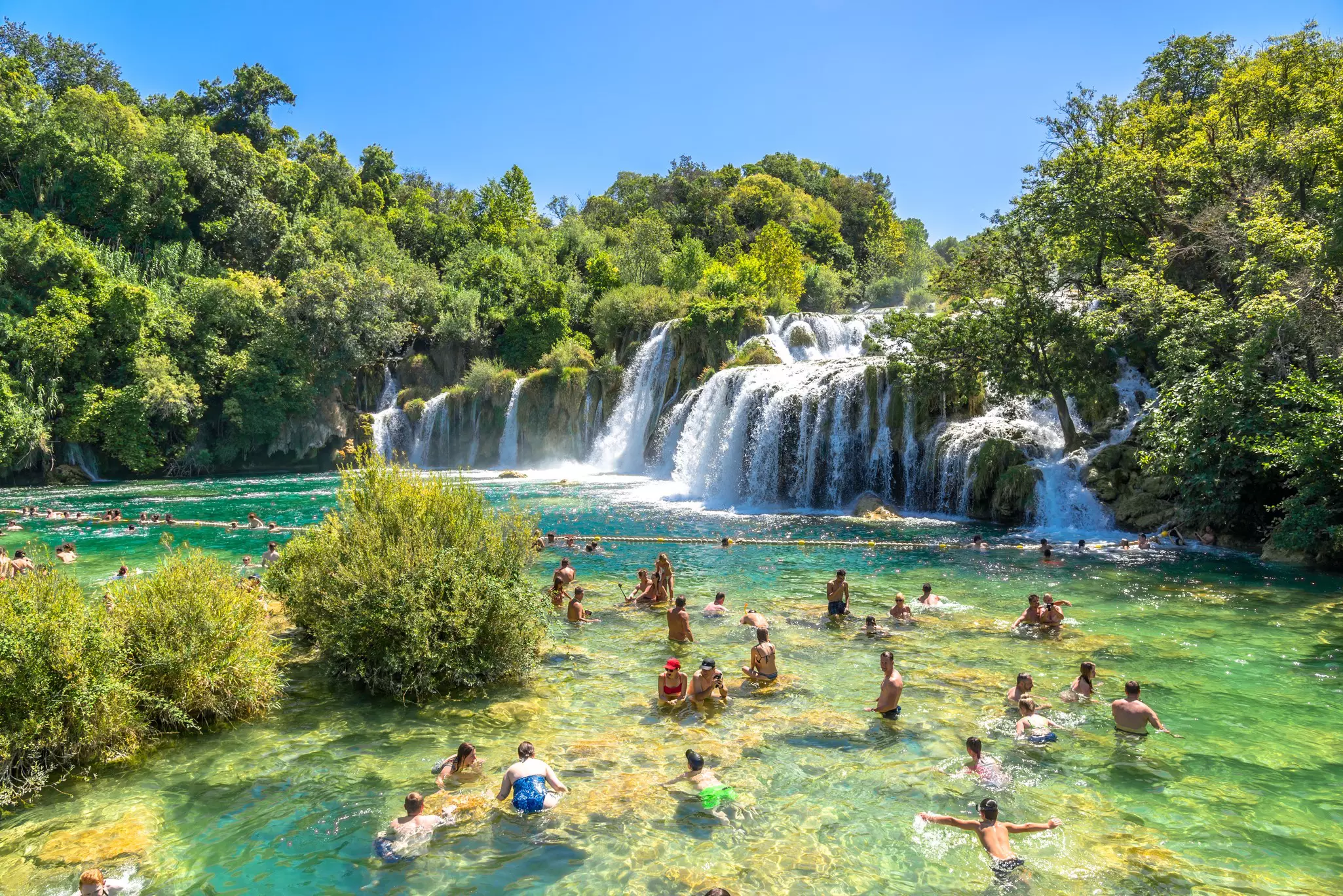 People swimming in clear greenish water by a waterfall in Croatia.
