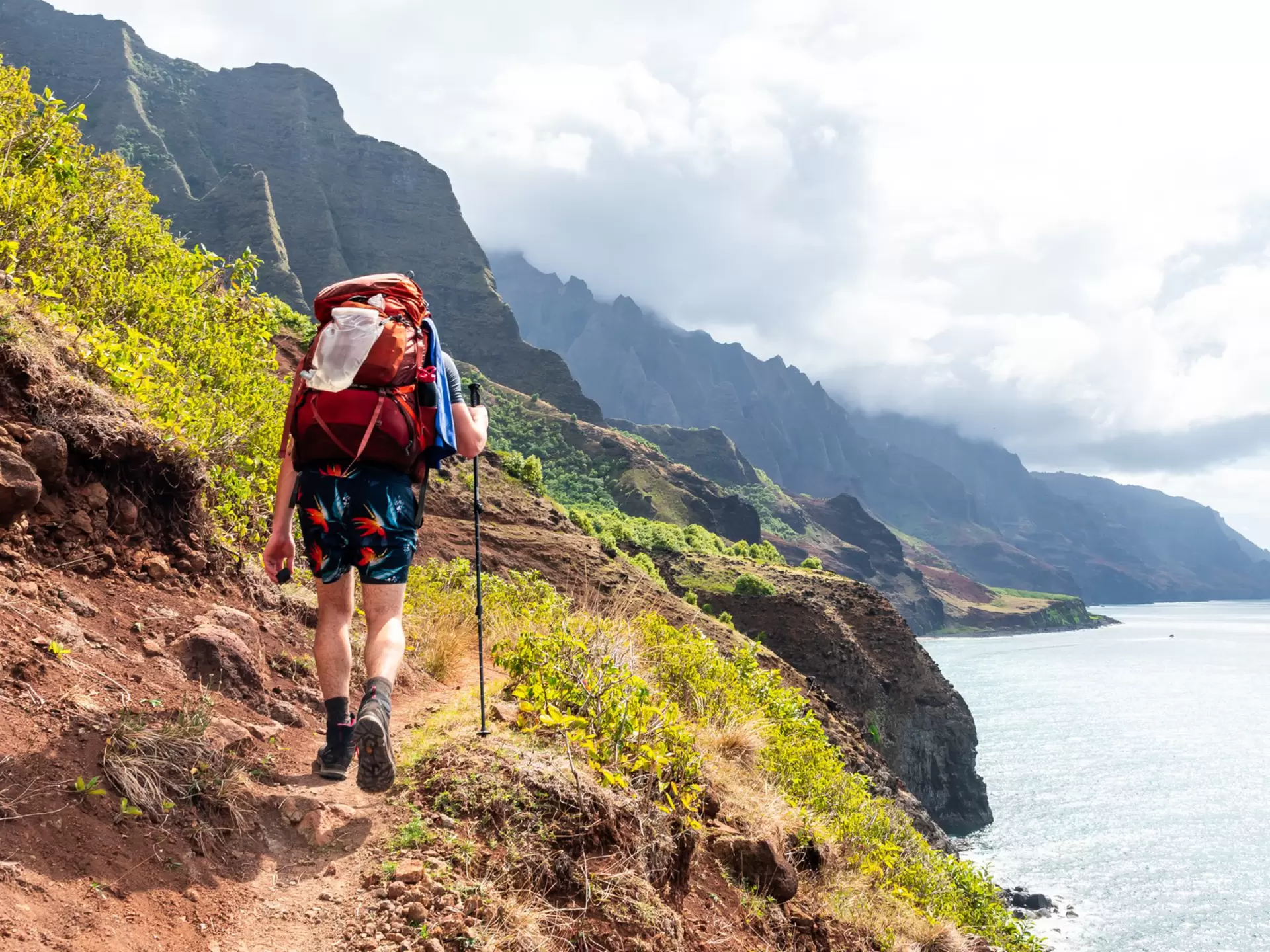 A hiker on a coastal trail high above the ocean: Kalalau Trail, Kauaʻi, Hawaiʻi