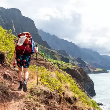 A hiker on a coastal trail high above the ocean: Kalalau Trail, Kauaʻi, Hawaiʻi