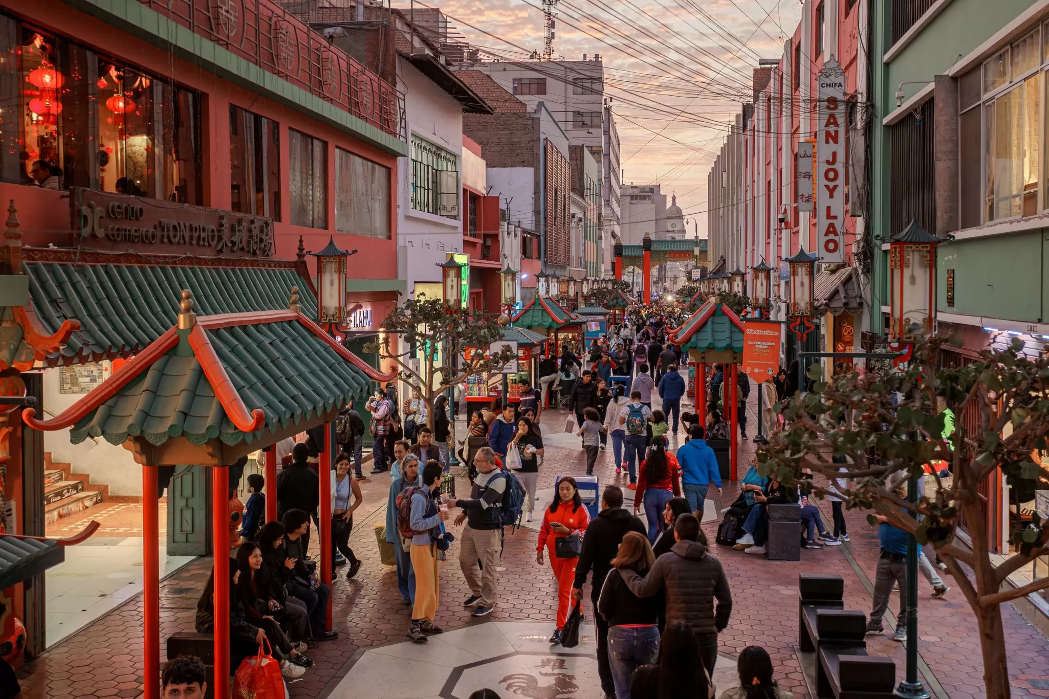 People walk down a pedestrianized street in a city at dusk.