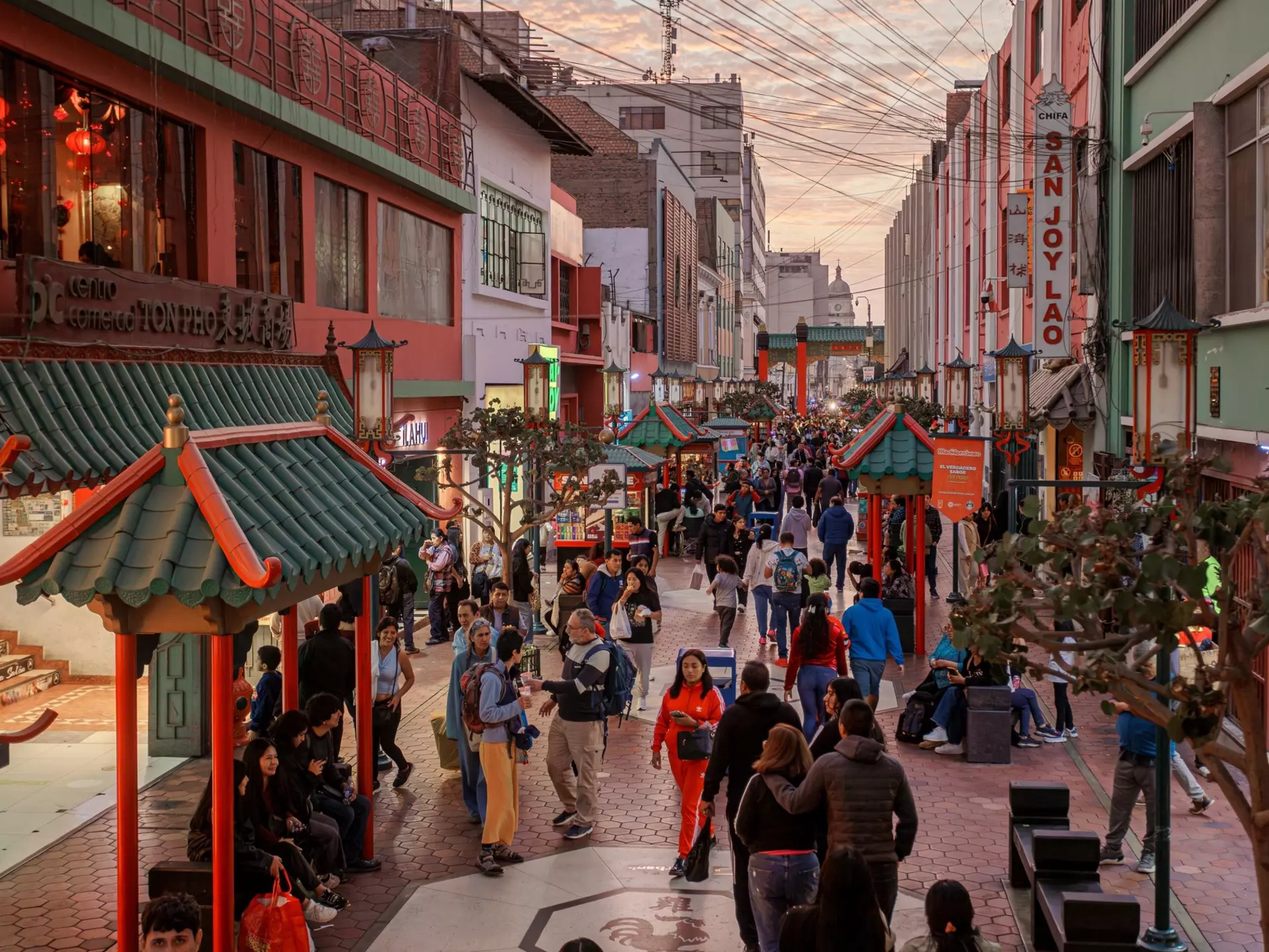 People walk down a pedestrianized street in a city at dusk.