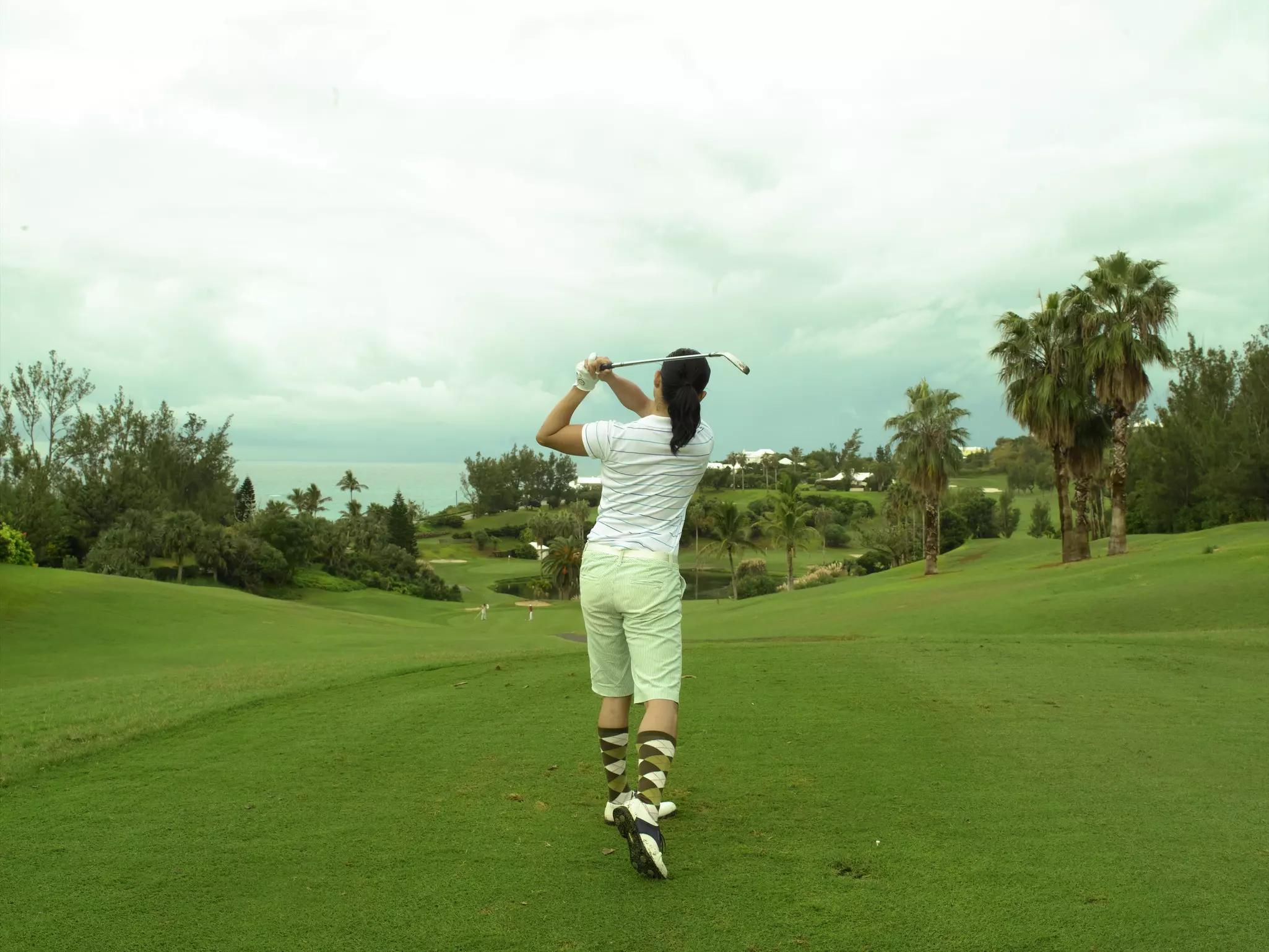 A woman taking a swing on a golf course under cloudy skies in Bermuda