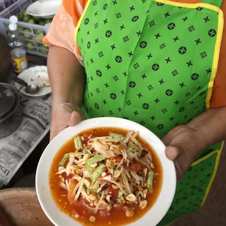 A woman in a green apron holds a plate of green payaya salad. 