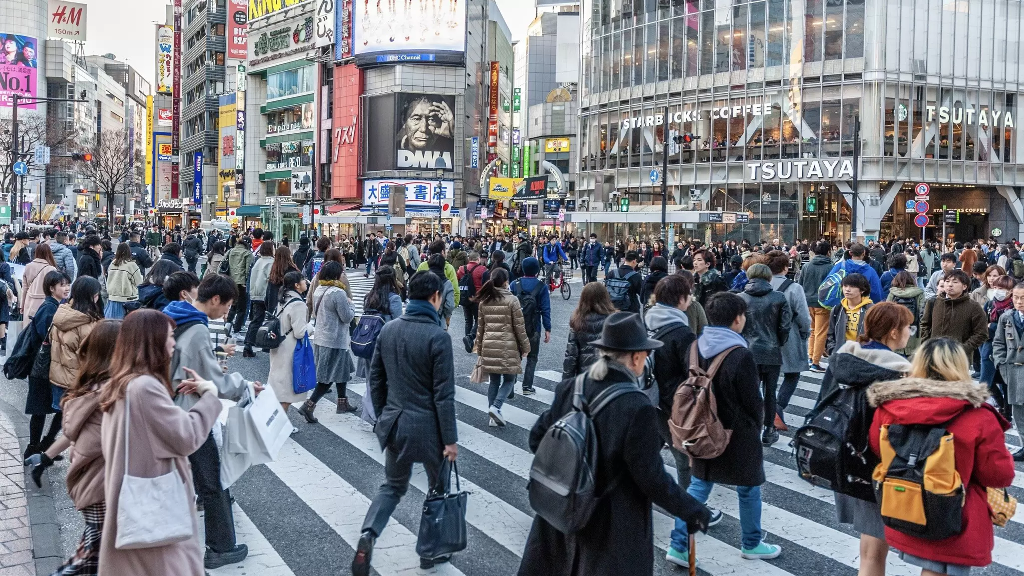 Many people walking along the busy streets and crossing at the famous Shibuya Crossing just around sunset.