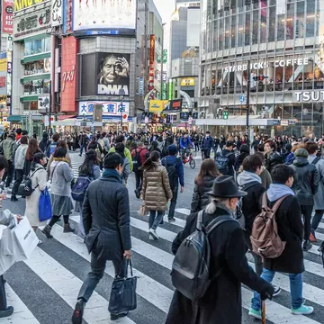 Many people walking along the busy streets and crossing at the famous Shibuya Crossing just around sunset.