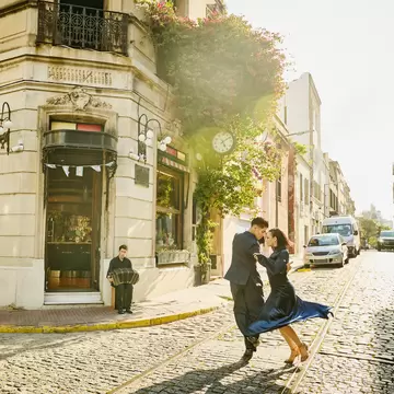 Two dancers performing the tango on a cobbled street as an accordion player plays nearby