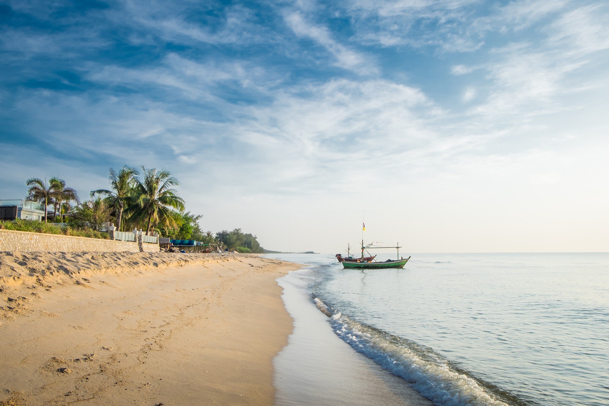 View of the turquoise waves with the blue sky and white clouds and fisherman's boat on a sandy beach in Hua Hin, Prachuap Khiri Khan Province, Thailand. 