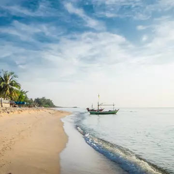 View of the turquoise waves with the blue sky and white clouds and fisherman's boat on a sandy beach in Hua Hin, Prachuap Khiri Khan Province, Thailand. 