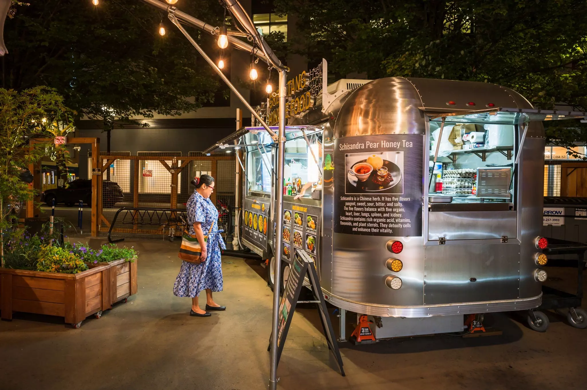 A woman stands at night in front of a vintage camping trailer converted into a food truck.