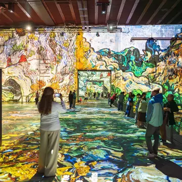 Visitors admiring large-scale digital projections of Van Gogh artworks at Les Bassins des Lumières, featuring vibrant colors and reflective floors in Bordeaux, France.