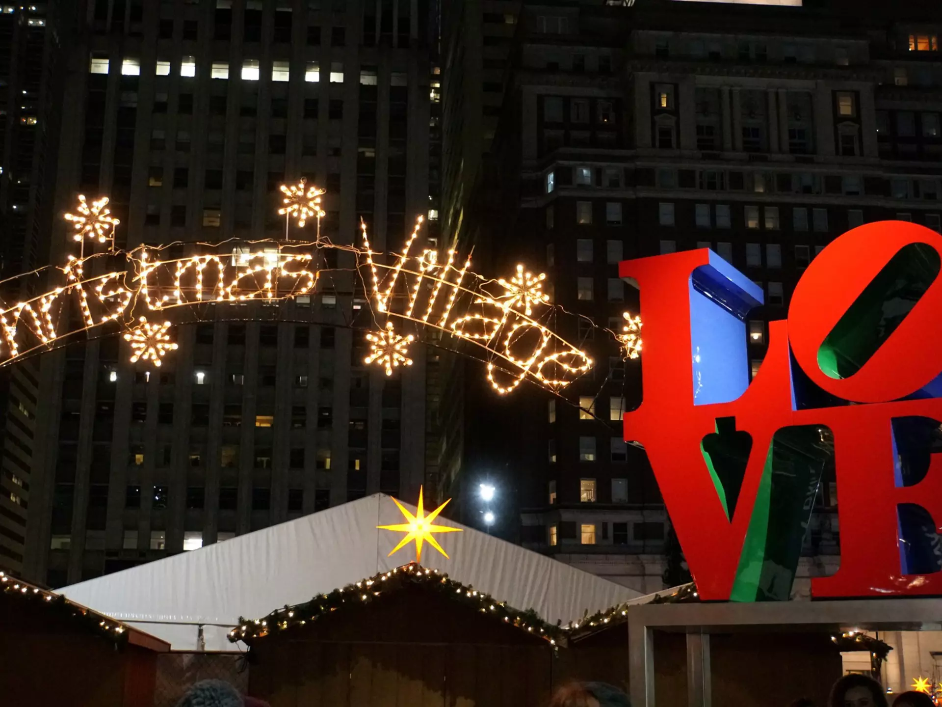 A large lit-up sign that reads "Christmas Village" next to a red sculpture spelling out the word "LOVE"