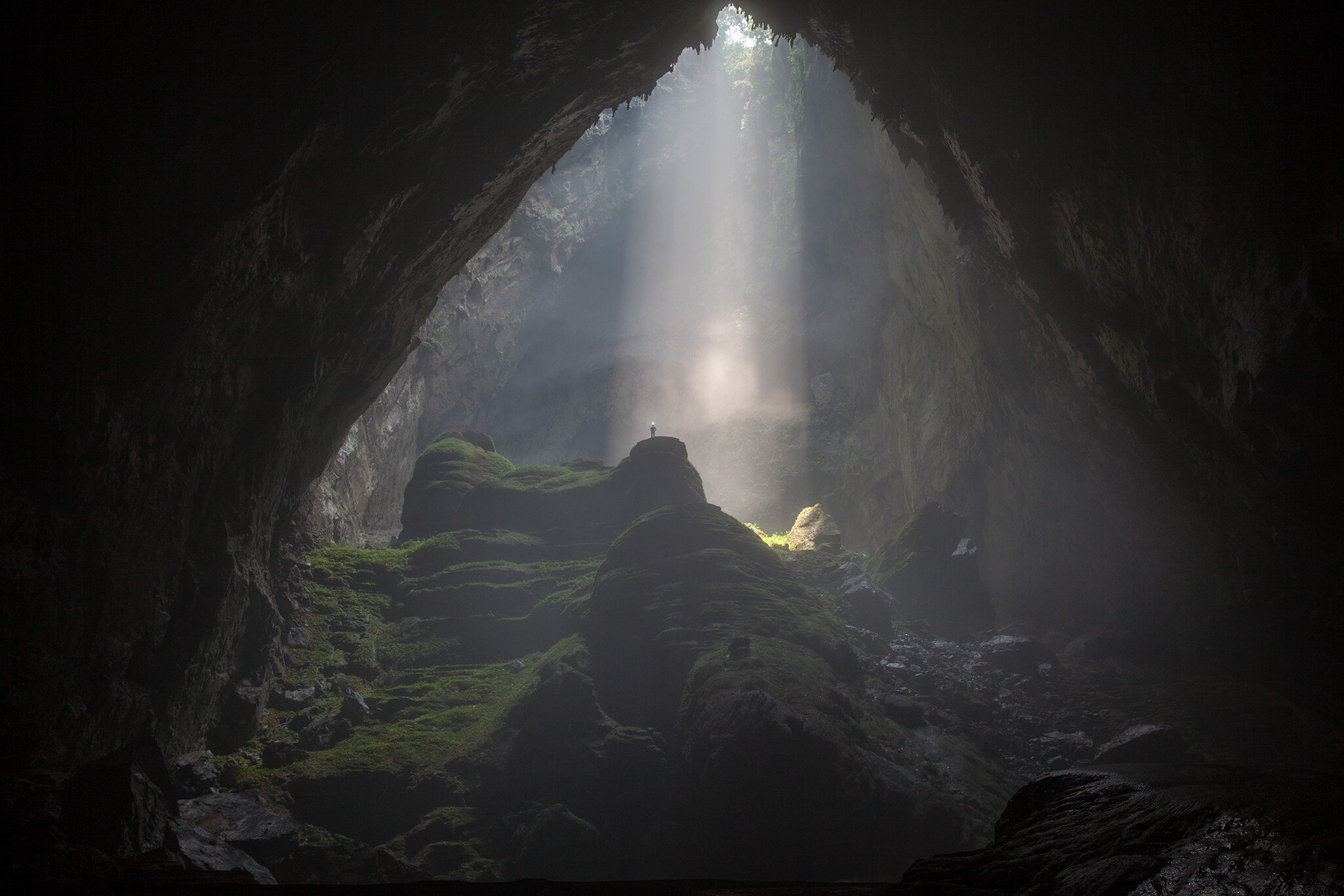 A person stands in a shaft of light flooding downwards into a vast cave system.