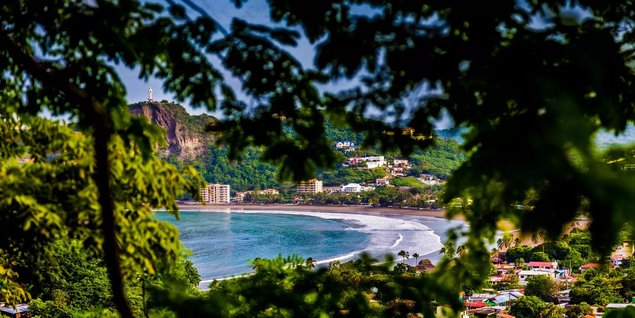 Waves lapping at a tropical beach in the center of a wide cove surrounded by lush foliage.