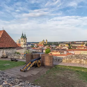 Old cannon and wicker baskets on a stone castle rampart above a town of red roofs and twin-towered churches, Eger, Hungary.