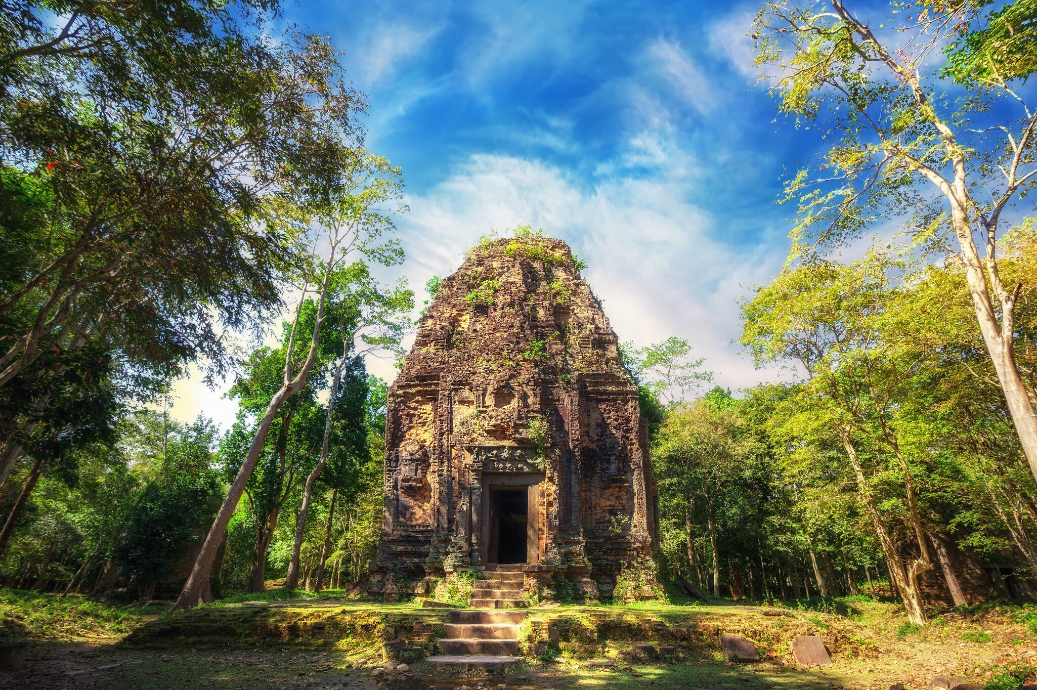 Ancient Khmer pre Angkor architecture. Sambor Prei Kuk temple ruins with giant banyan trees under blue sky.
