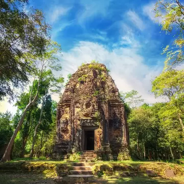 Ancient Khmer pre Angkor architecture. Sambor Prei Kuk temple ruins with giant banyan trees under blue sky.