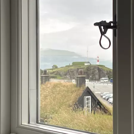 A framed window pane through which you can see sod roofed houses and a lighthouse in the distance.