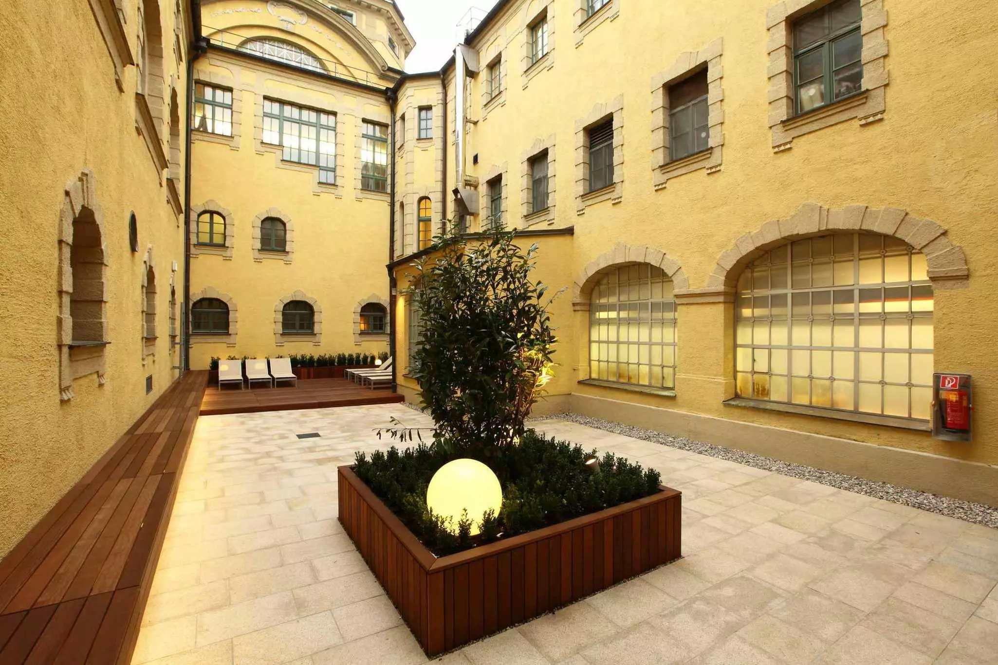 A fully enclosed courtyard with a wooden bench running down one side. Loungers are placed on the decking.