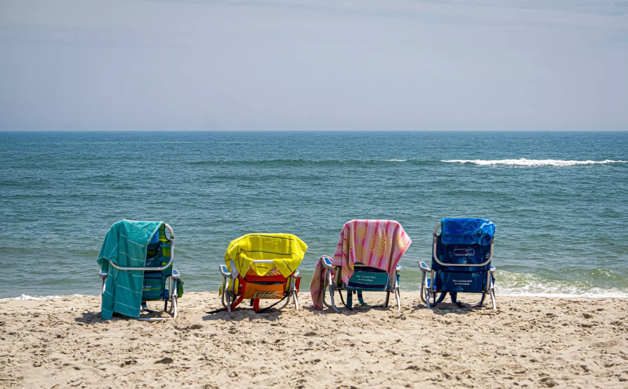 Four beach chairs on a sandy beach facing the ocean.