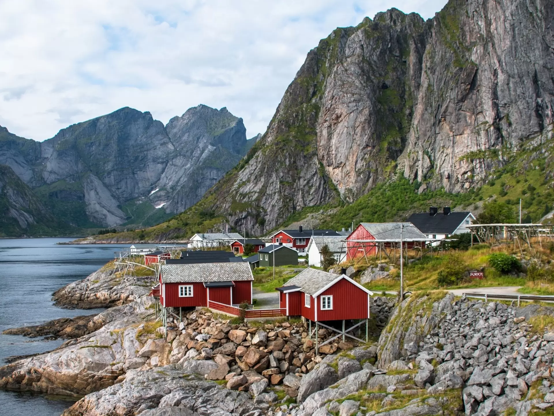small red wooden houses sit on a rocky shoreline with mountains in the background