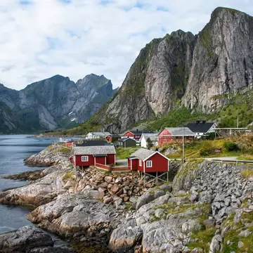 small red wooden houses sit on a rocky shoreline with mountains in the background
