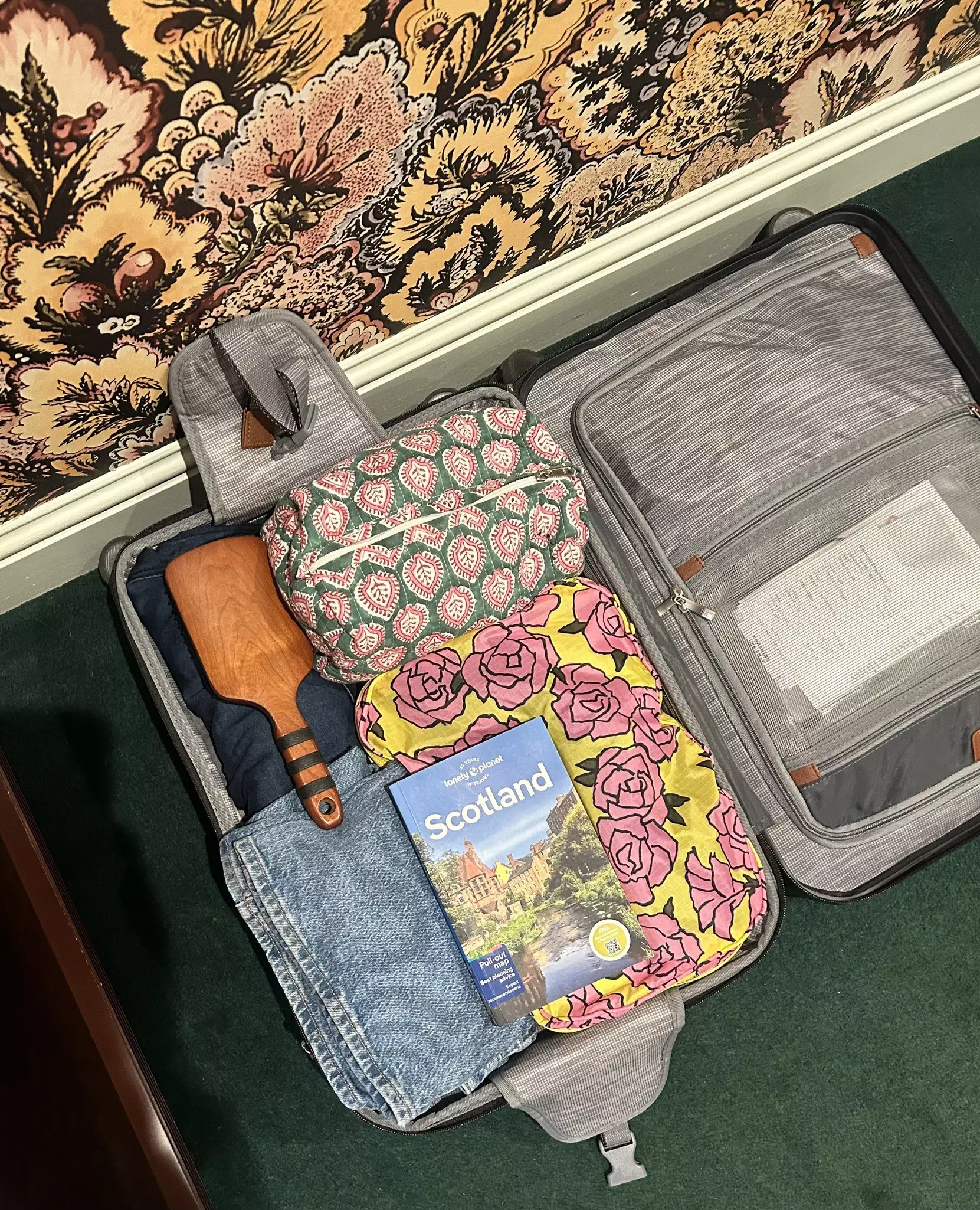 A suitcase packed with clothing, a guidebook, a hairbrush and other smaller bags.