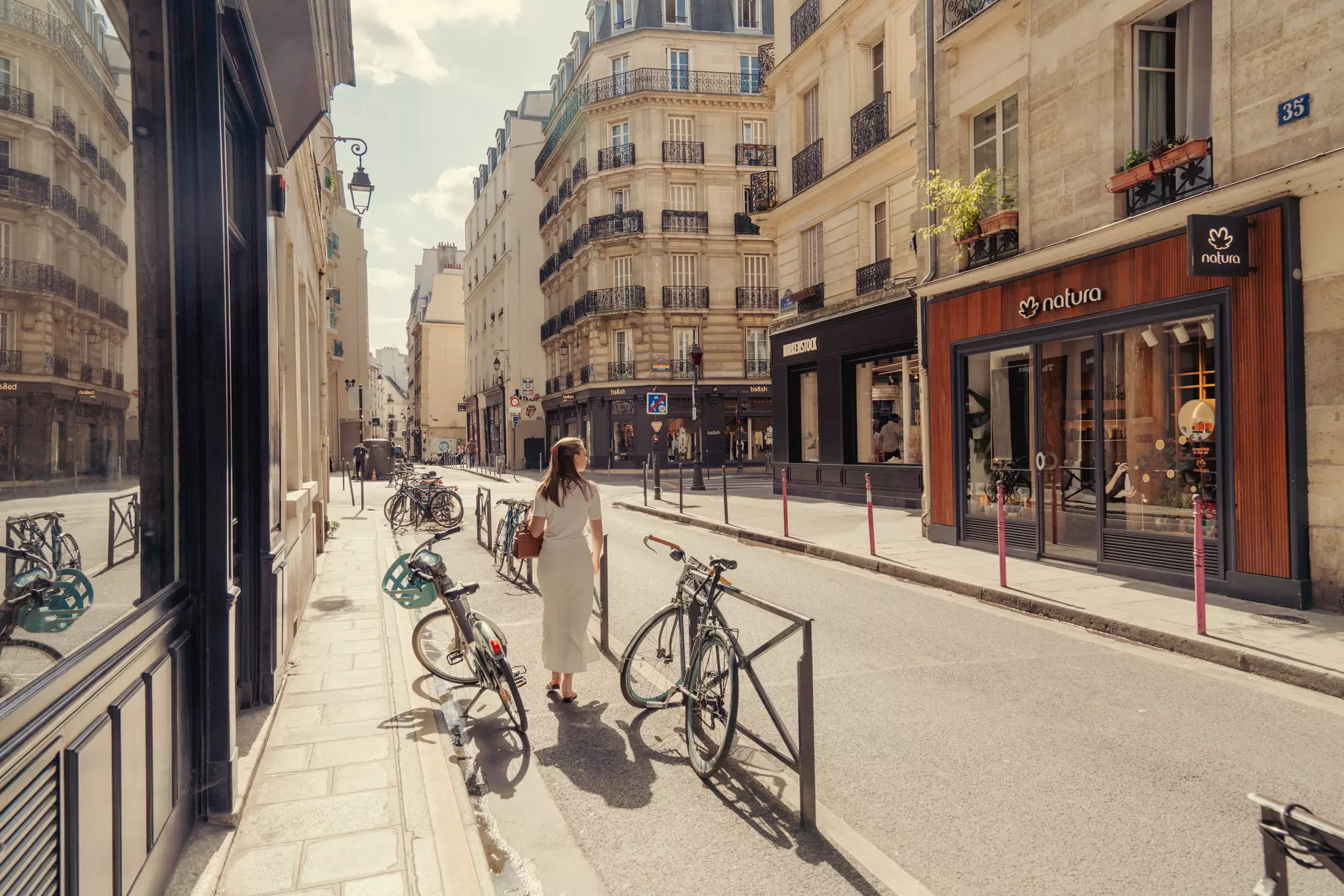 A person walking on an empty sidewalk with bicycles in bright sunlight.