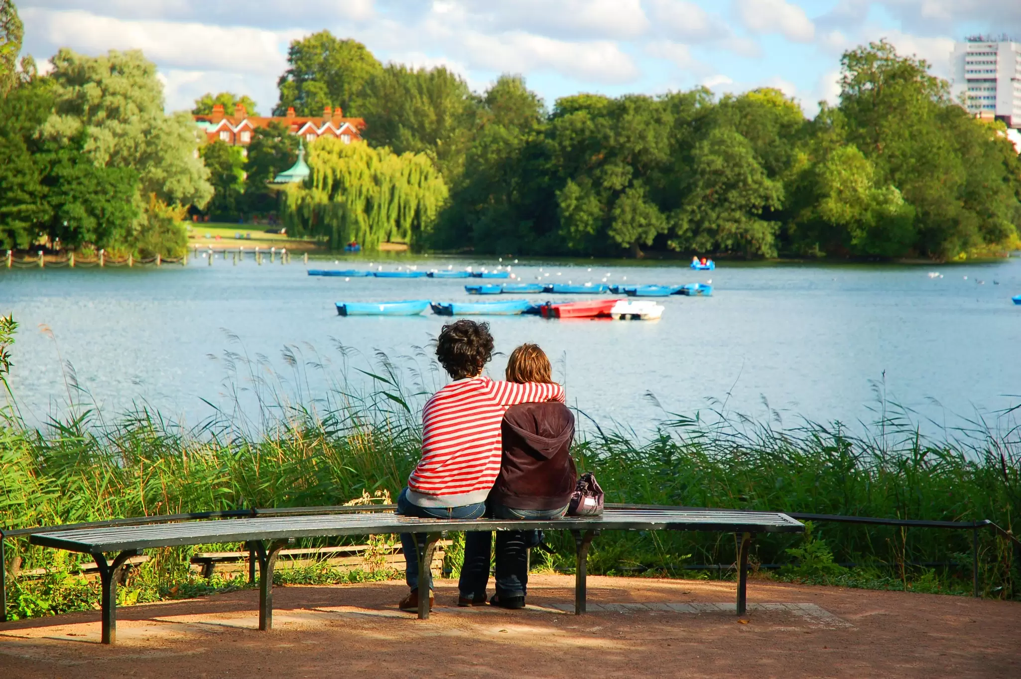 People sitting on a bench looking at the boating lake at Regent's Park in London, UK