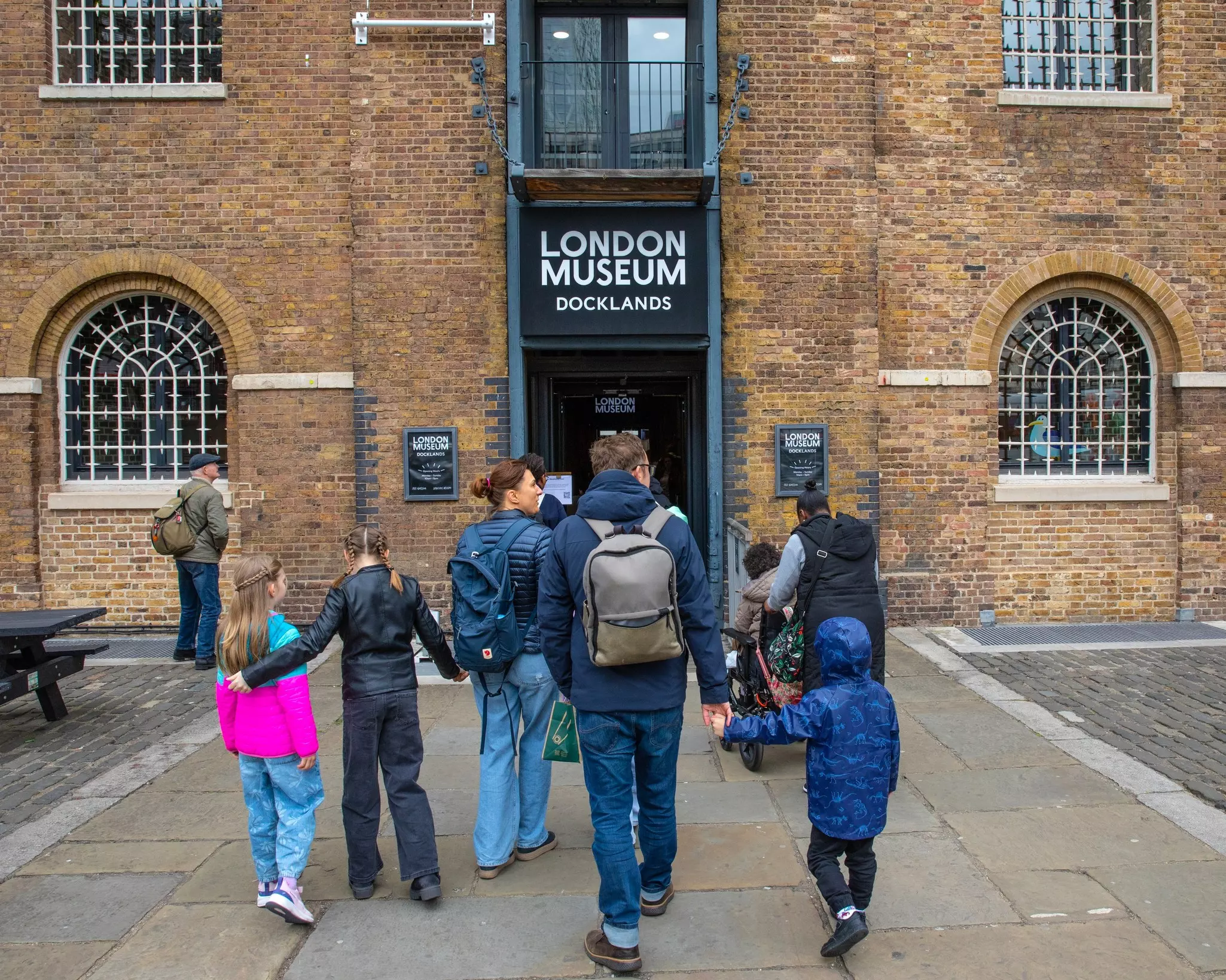 A large brick warehouse building that's been converted into a museum. A group of adults and children approach the entrance.