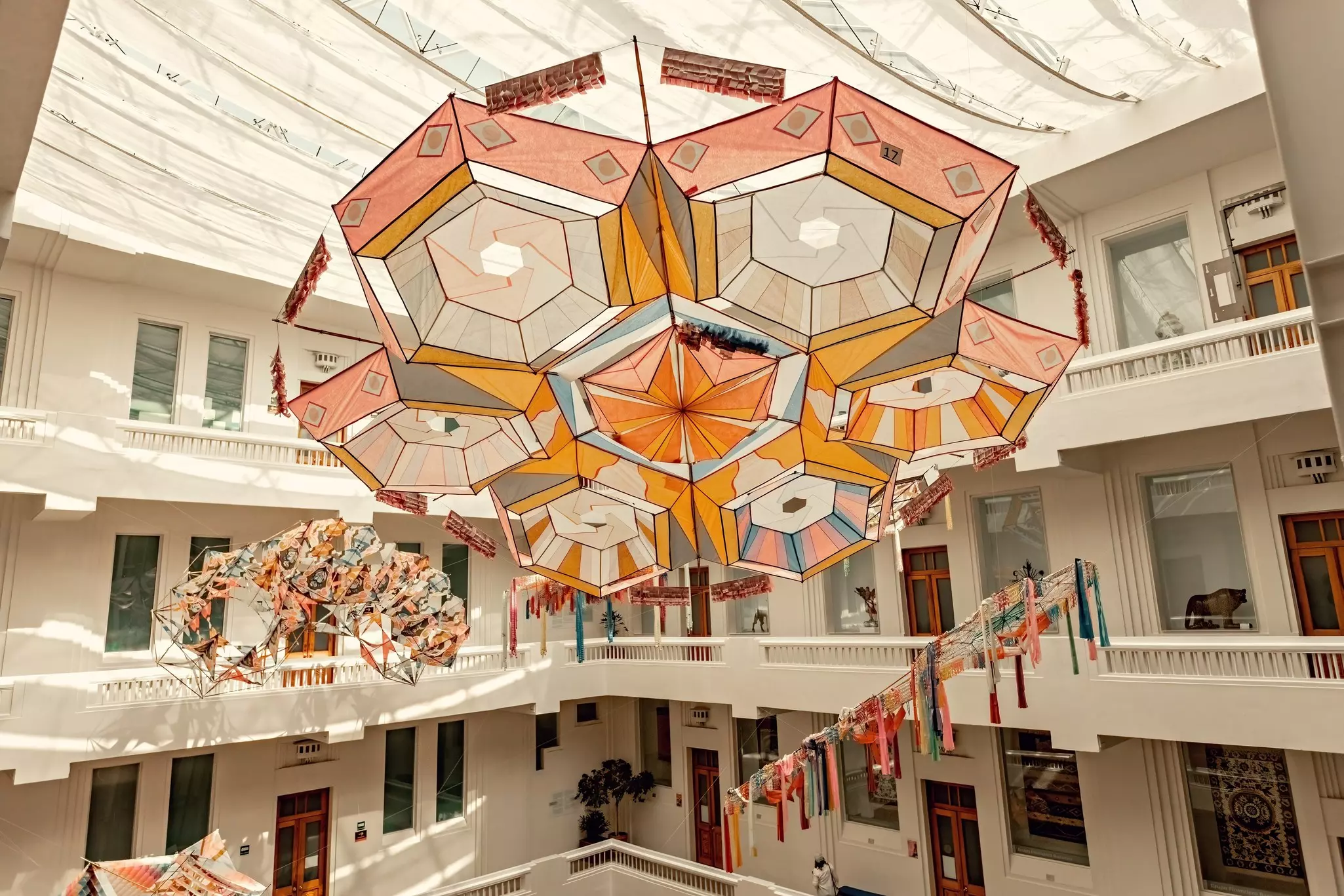 A large sculpture made of fabric in geometric shapes hangs from a ceiling in a central atrium of a museum