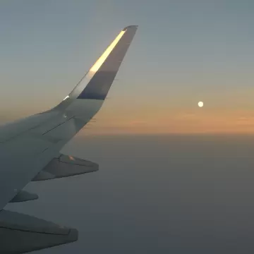 An airplane wing in flight and the moon at sunset.