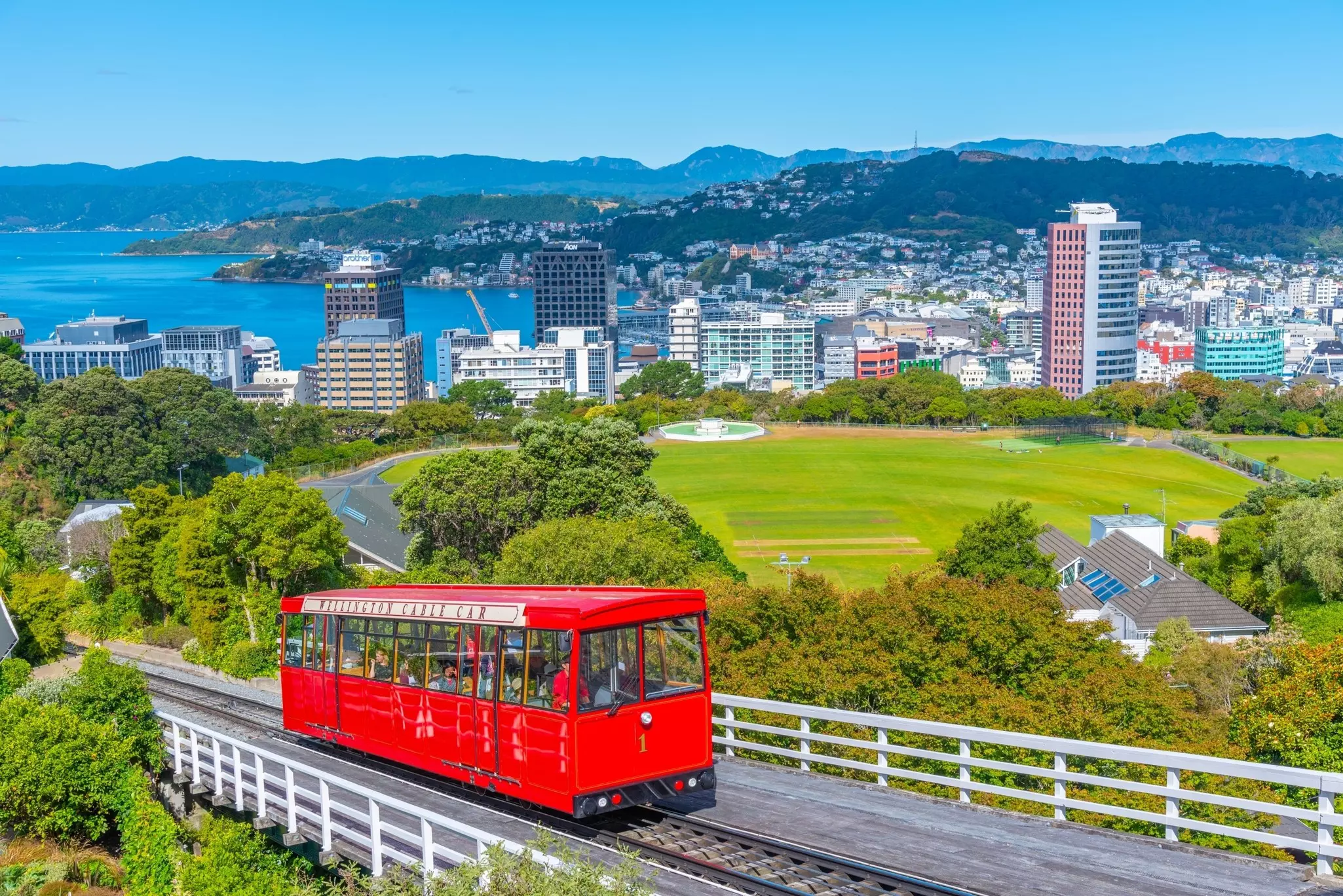 A red cable car carriage travels uphil on a track in a harbor city.